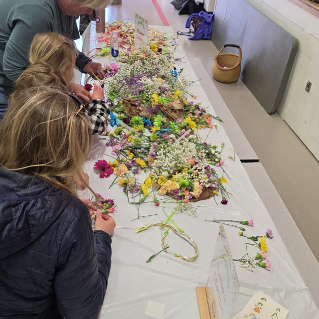 A table of fresh flowers where families weave flower crowns before the dance