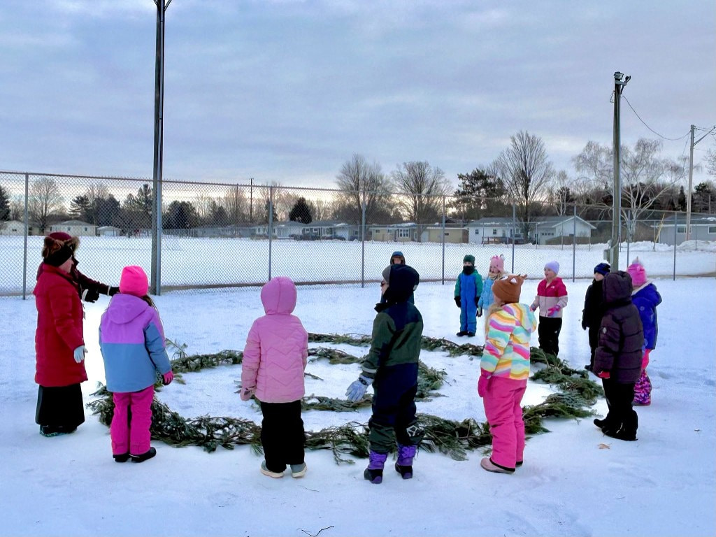 Children gathered around an evergreen spiral laid in the snow for the Spiral Walk