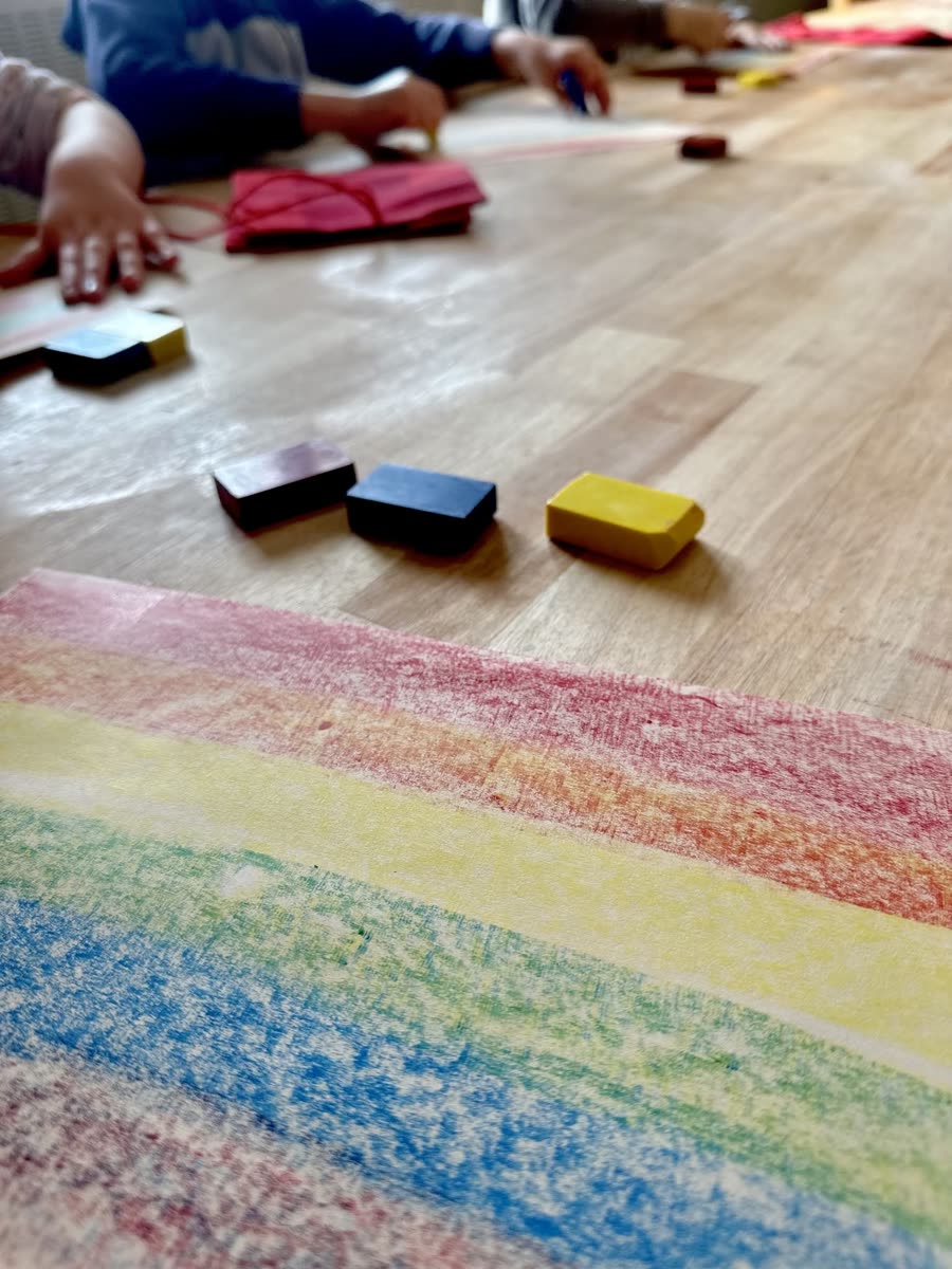 Beeswax block crayons beside a rainbow drawn in broad bands of colour