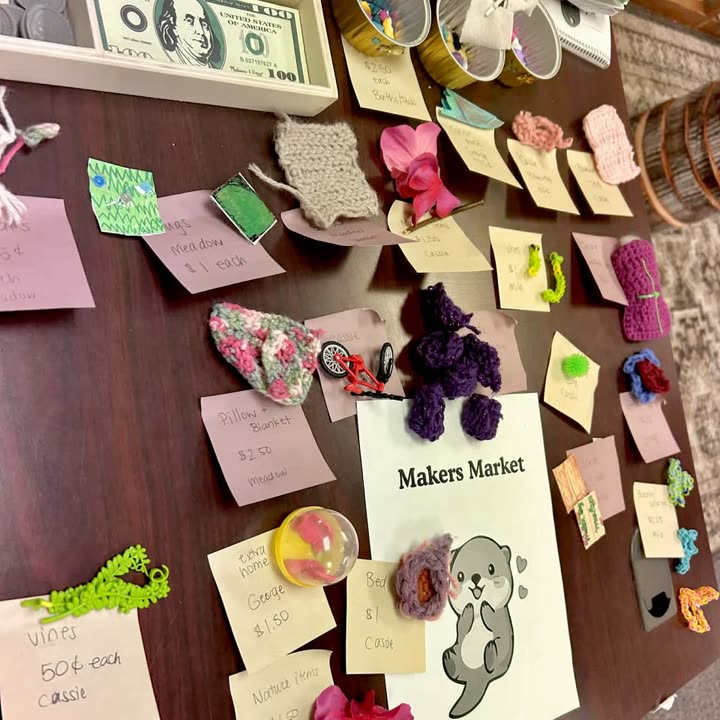 A Makers Market table of knitted and felted goods with hand-lettered price cards made by students