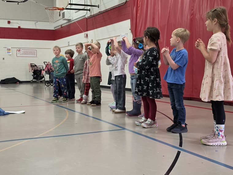 A class standing together with hands raised, speaking a verse with their teacher