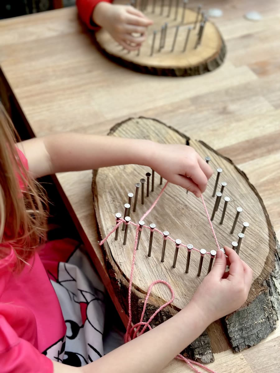 A student threading pink string between nails hammered around a slice of tree trunk