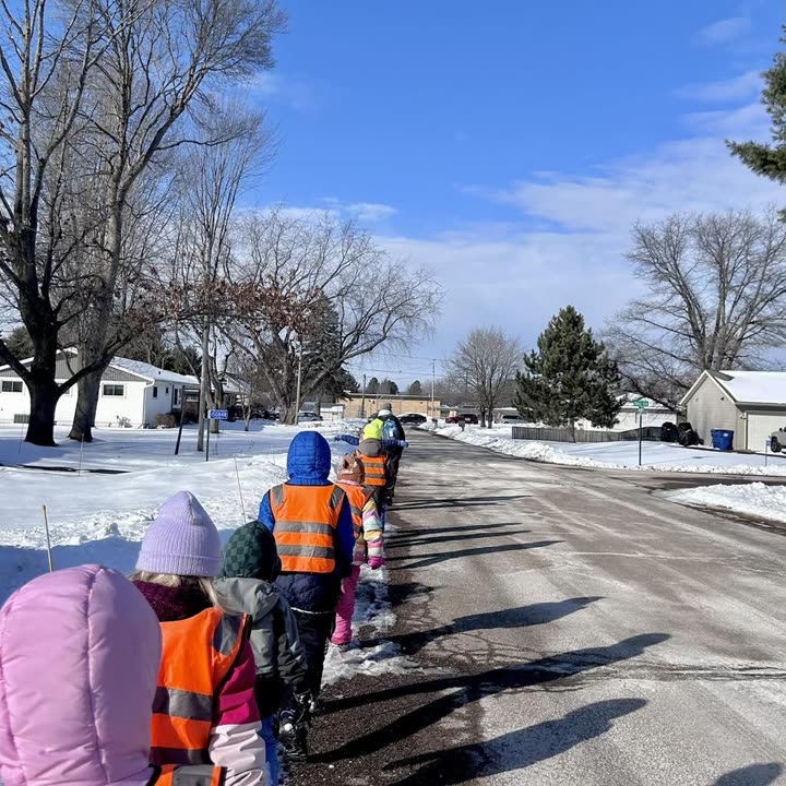 Students in high-visibility vests and winter coats walking single file along a snowy neighbourhood road
