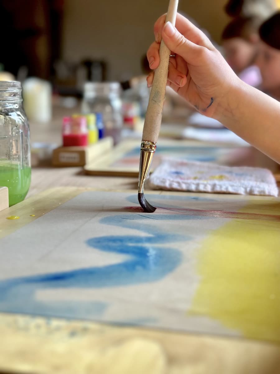 A student laying a stroke of blue watercolour beside yellow on wet paper